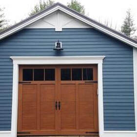 Haas American TraditionCarriage House steel garage door in wood tone color with rectangular windows and black decorative hardware 